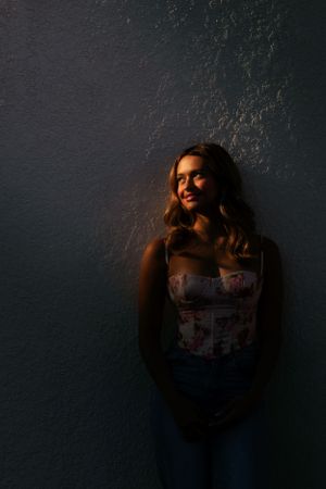 Moody portrait against dark wall with dramatic side lighting.