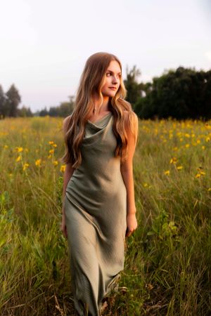 A flowing olive green dress creates movement in a field of yellow wildflowers at sunset.
