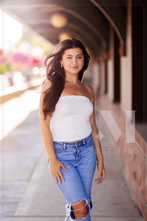 Casual fashion photoshoot in a covered walkway featuring white top and distressed blue jeans.