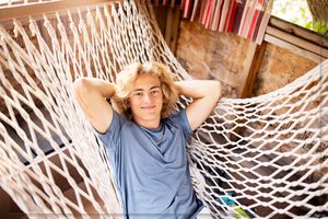 Person lounging in a cozy rope hammock during a sunny afternoon with trees in the background.