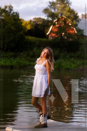 A sunny outdoor photoshoot on a dock by the water showing someone in a white summer dress.