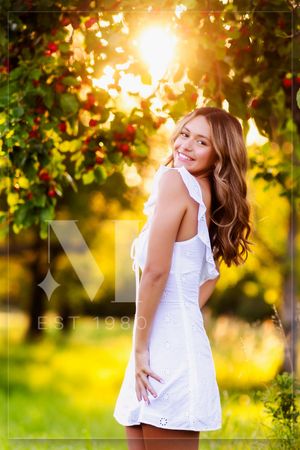 A figure in a white dress twirls playfully in a sunlit garden setting during golden hour.