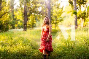 A person in a flowing red dress twirls joyfully in a sunlit meadow with golden wildflowers and trees.