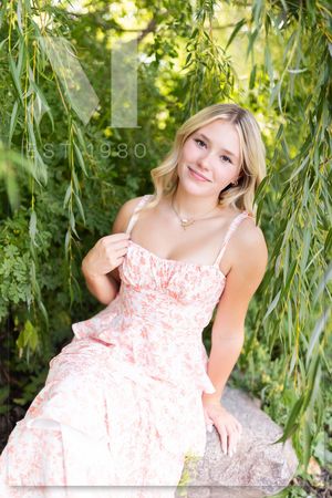 A pastoral portrait scene with willow tree branches framing someone in a coral floral sundress on a warm summer day.