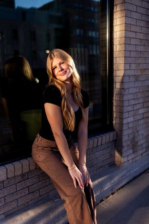Person in casual wear poses against a brick wall during golden hour lighting.