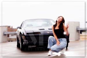 An indoor studio photography session with minimalist white interior and modern luxury cars in the background.