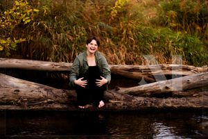 A figure sits perched on a fallen log by a serene stream against an autumn woodland backdrop.