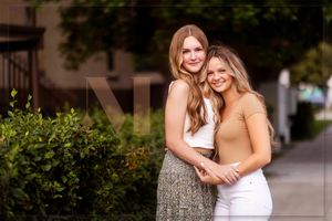 Two people embrace while standing outdoors near green bushes on a sunny day.