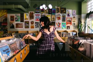 Person browsing through vinyl records at a music store with posters covering the walls.