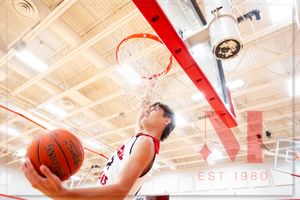 Basketball player leaps high for a layup shot under a bright indoor gymnasium hoop.