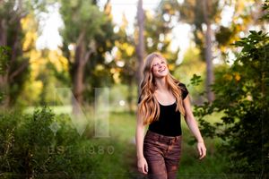 Person joyfully walking through a lush green path during sunset, wearing casual attire.