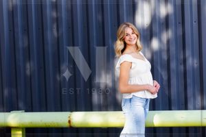 A person in blue jeans and a white crop top poses against a blue industrial wall with dramatic lighting.