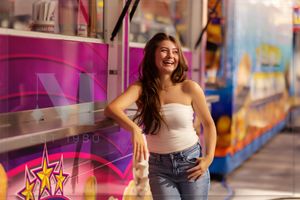 Woman in white tube top and jeans poses cheerfully in front of colorful food truck with vibrant pink and purple lighting.