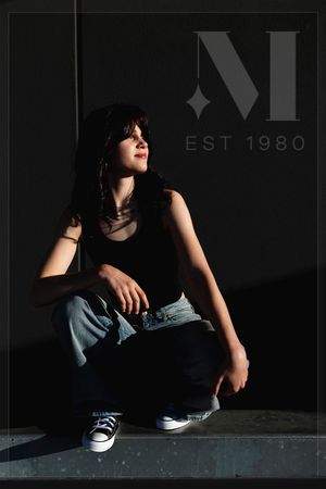 Dramatic portrait against a dark wall with 'EST 1980' signage in moody lighting.