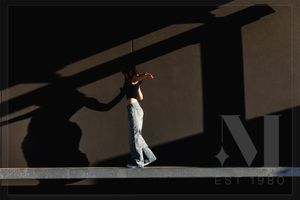 A silhouette walks along a wall casting dramatic shadows in minimalist monochrome composition.