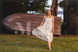 A flowing white sundress billows in the breeze as someone stands on a grassy lawn at sunset.