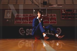 Dancer in a blue tracksuit performs a breakdancing move on a polished basketball court floor.