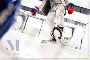Close-up action shot of hockey player making sharp turn on ice, spraying snow with skates during intense gameplay.