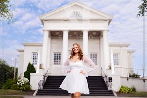 A white neoclassical building with columns serves as backdrop for a photo on its grand entrance steps.