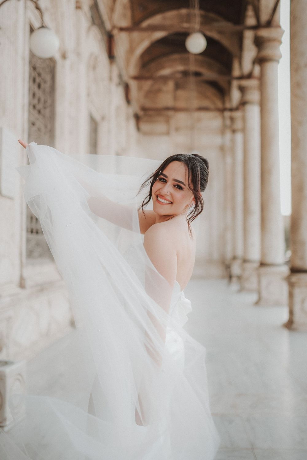 Ethereal bridal portraits in an elegant colonnade with flowing white veil creating dreamy movement and atmosphere.