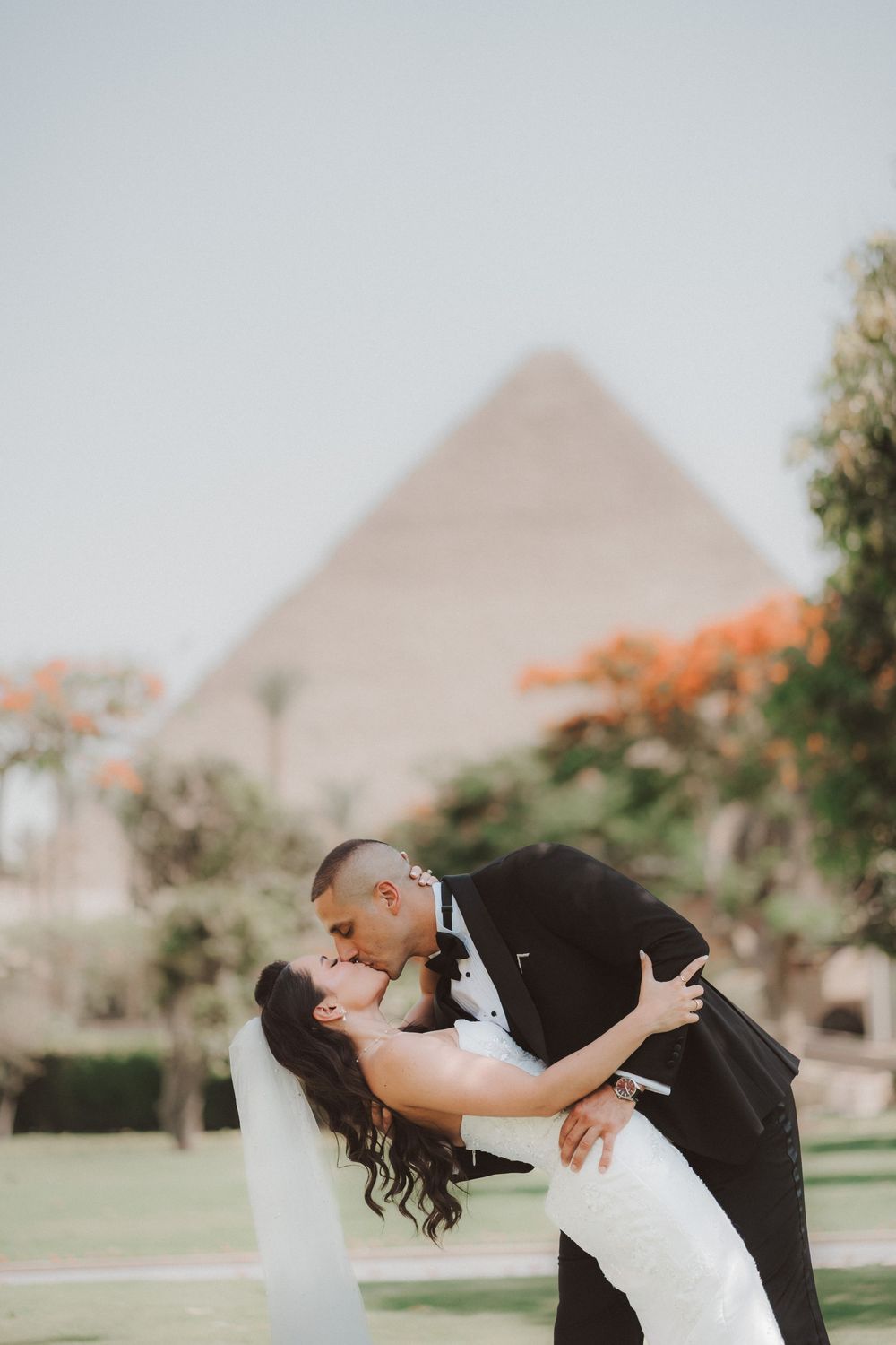 A romantic wedding couple shares a kiss in front of the Great Pyramid of Giza in Egypt.