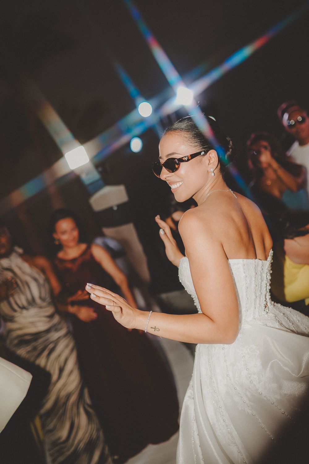 Person in a white dress dancing at a nightclub with colorful lights in the background.