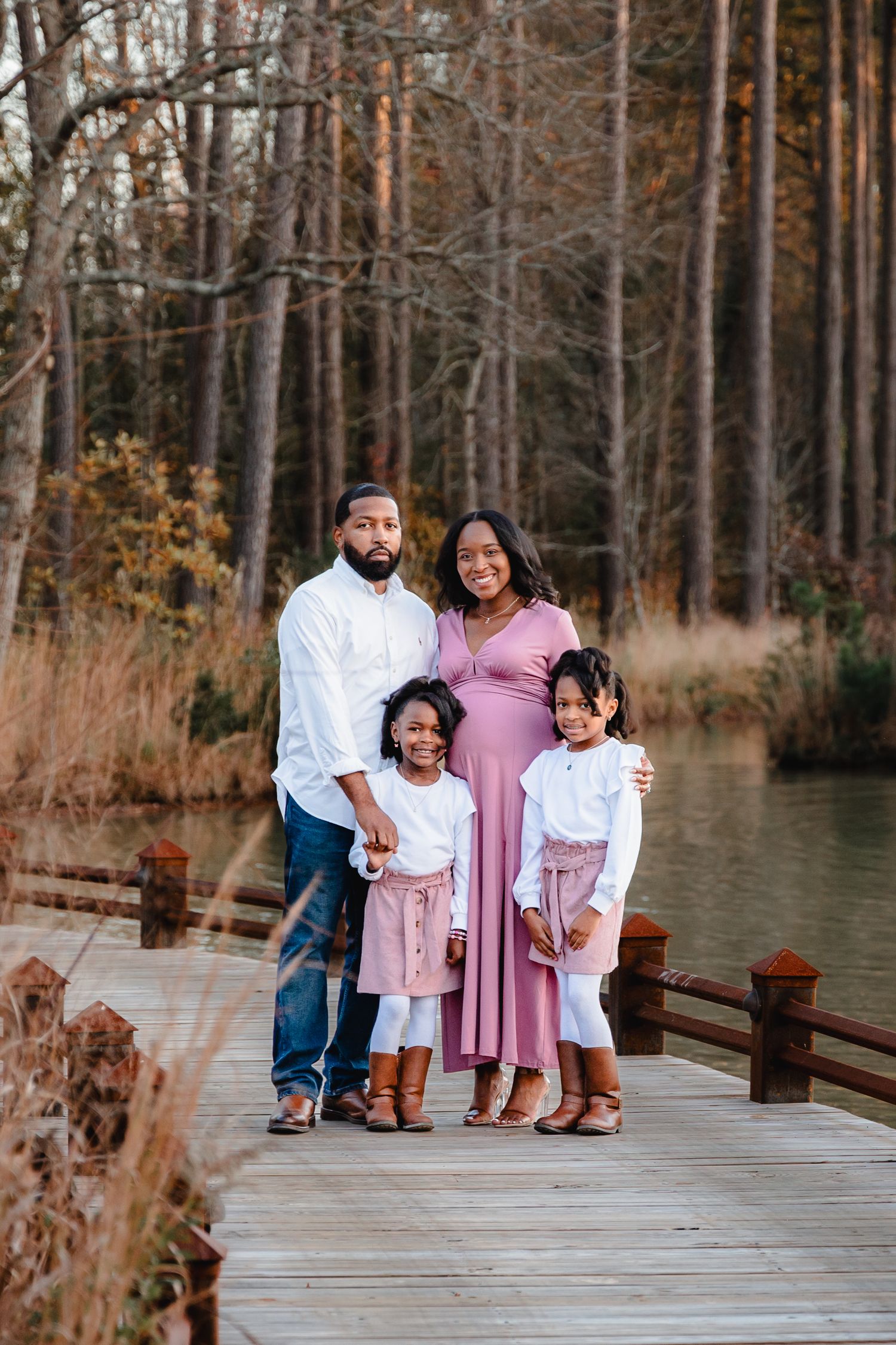 Family of four posing together on wooden boardwalk surrounded by autumn trees.