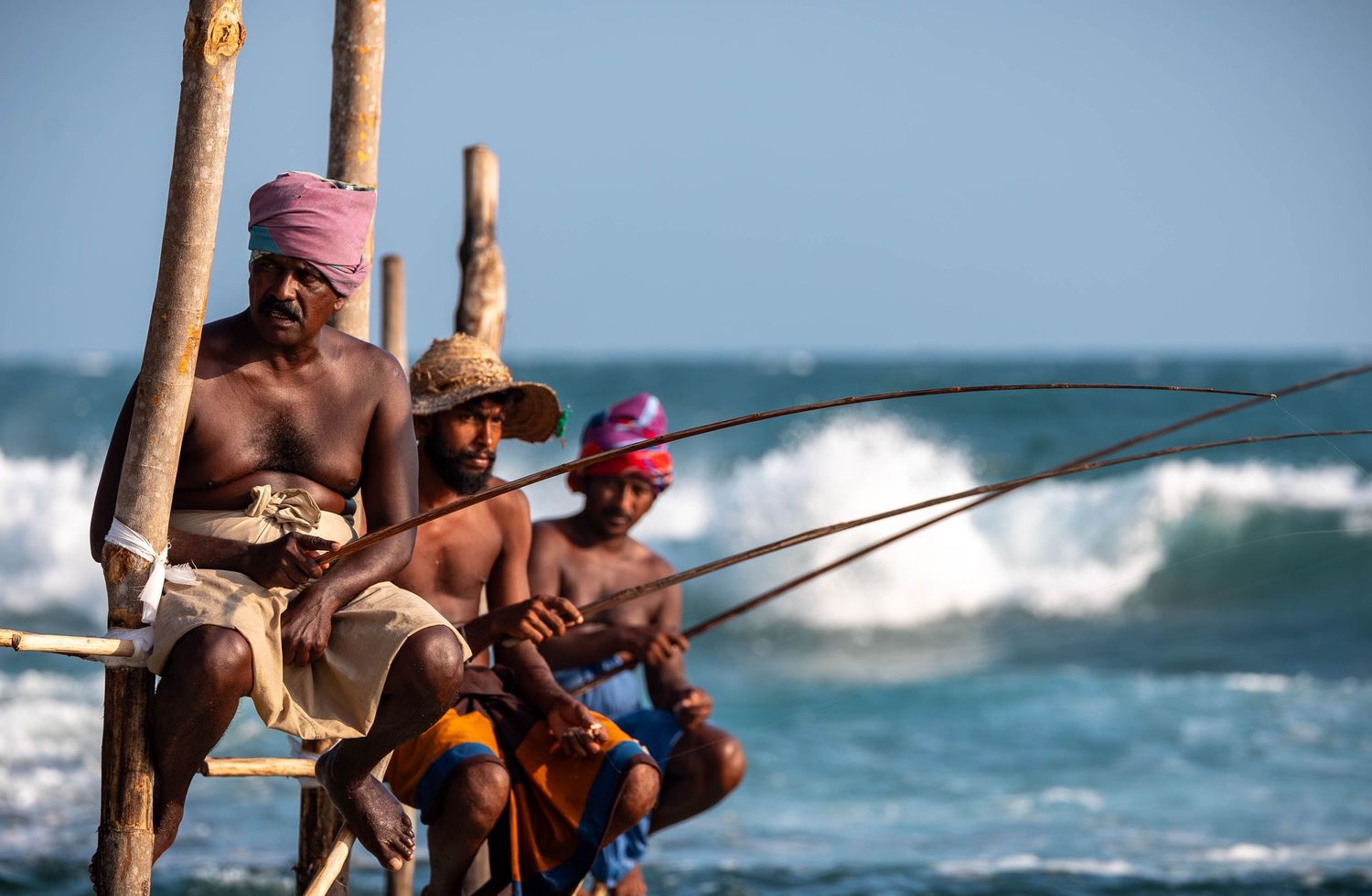 Traditional stilt fishermen cast their lines from poles in the crashing ocean waves.