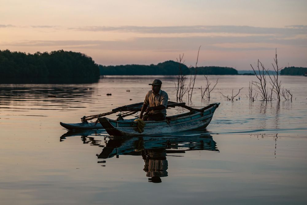 Silhouette of fisherman in small boat on tranquil lake during sunset.