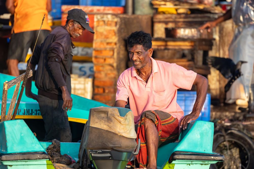 Two people having a conversation while sitting on a turquoise boat outside the fish market in Sri Lanka.