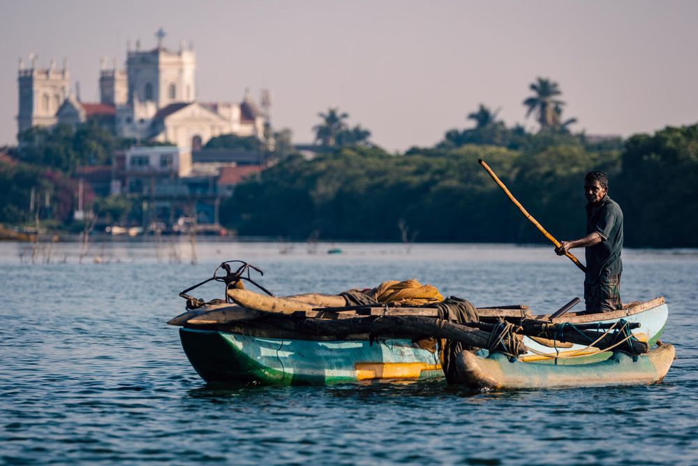 A silhouetted figure fishes from a small boat with a church visible in the background in Sri Lanka.