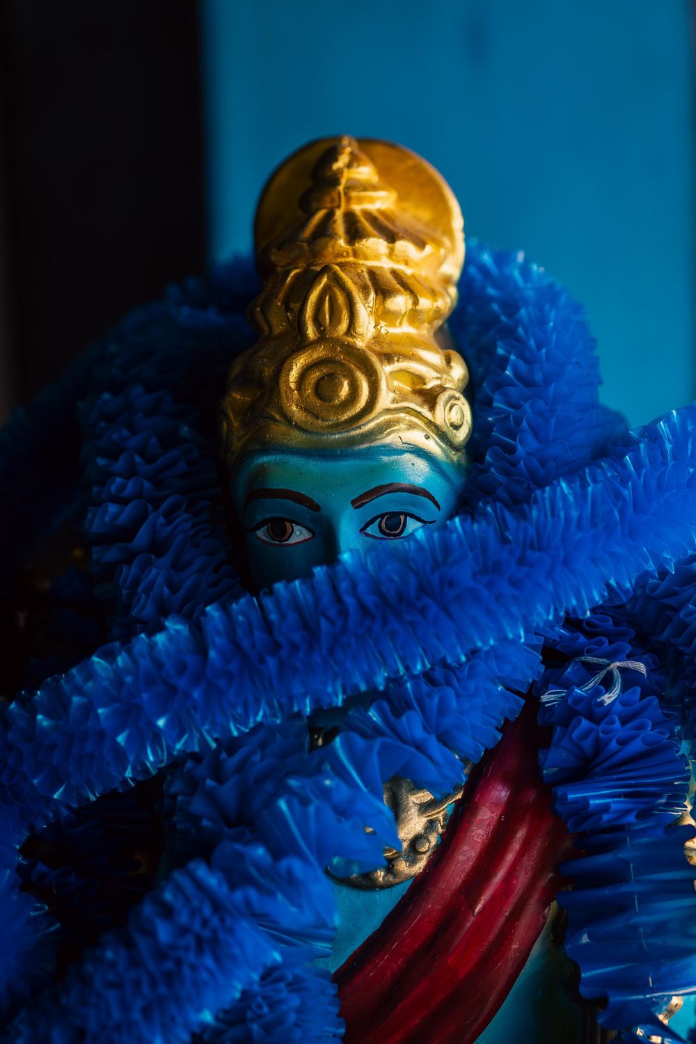 Traditional Indian deity figurine with ornate golden crown and blue decorative elements.