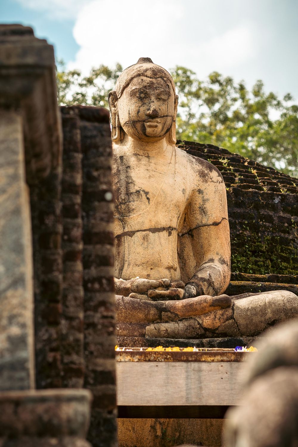 Ancient stone Buddha statue sitting in meditation pose at historic ruins in Sri Lanka.