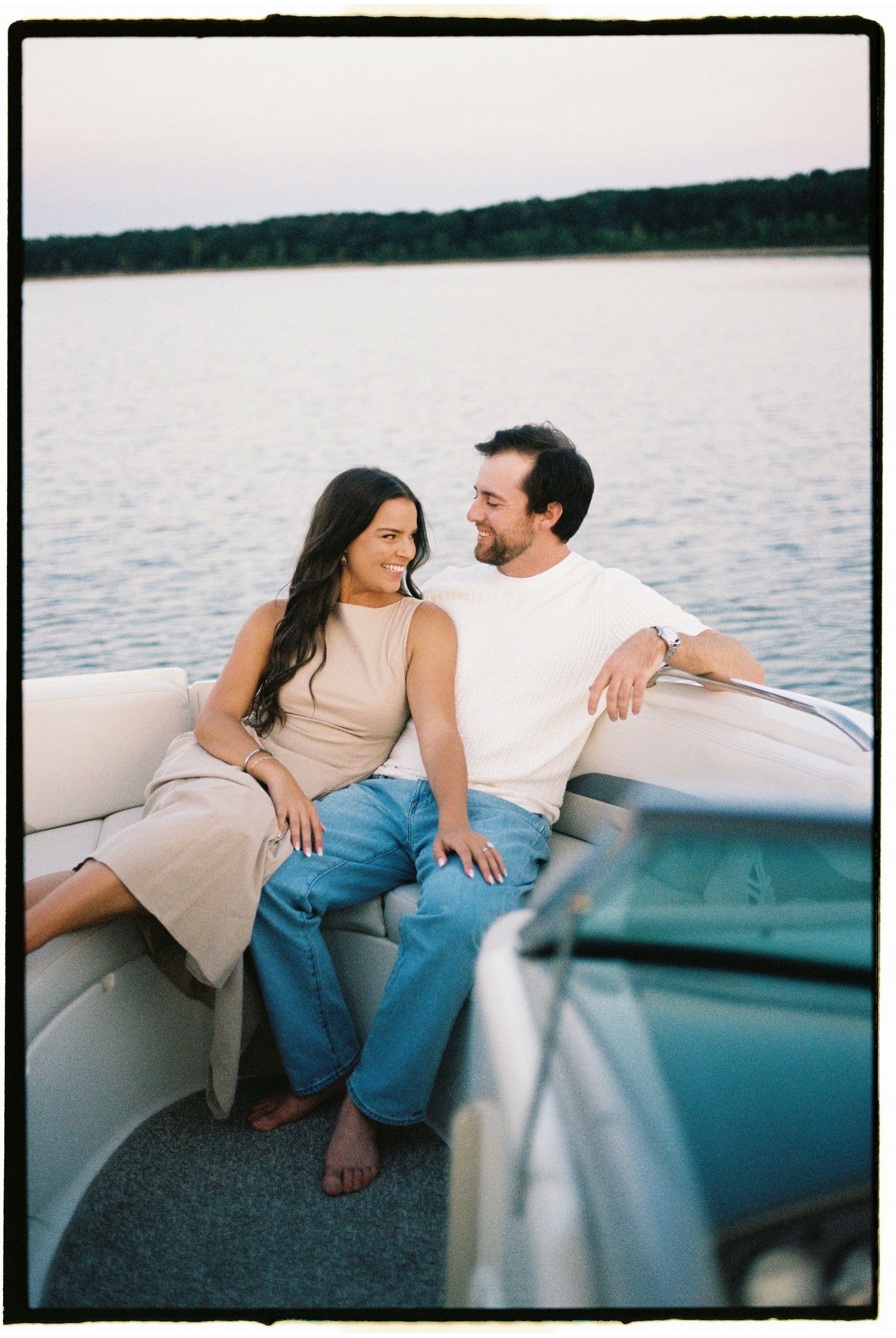A couple sits close together on a boat at dusk, enjoying a peaceful moment on the calm lake.