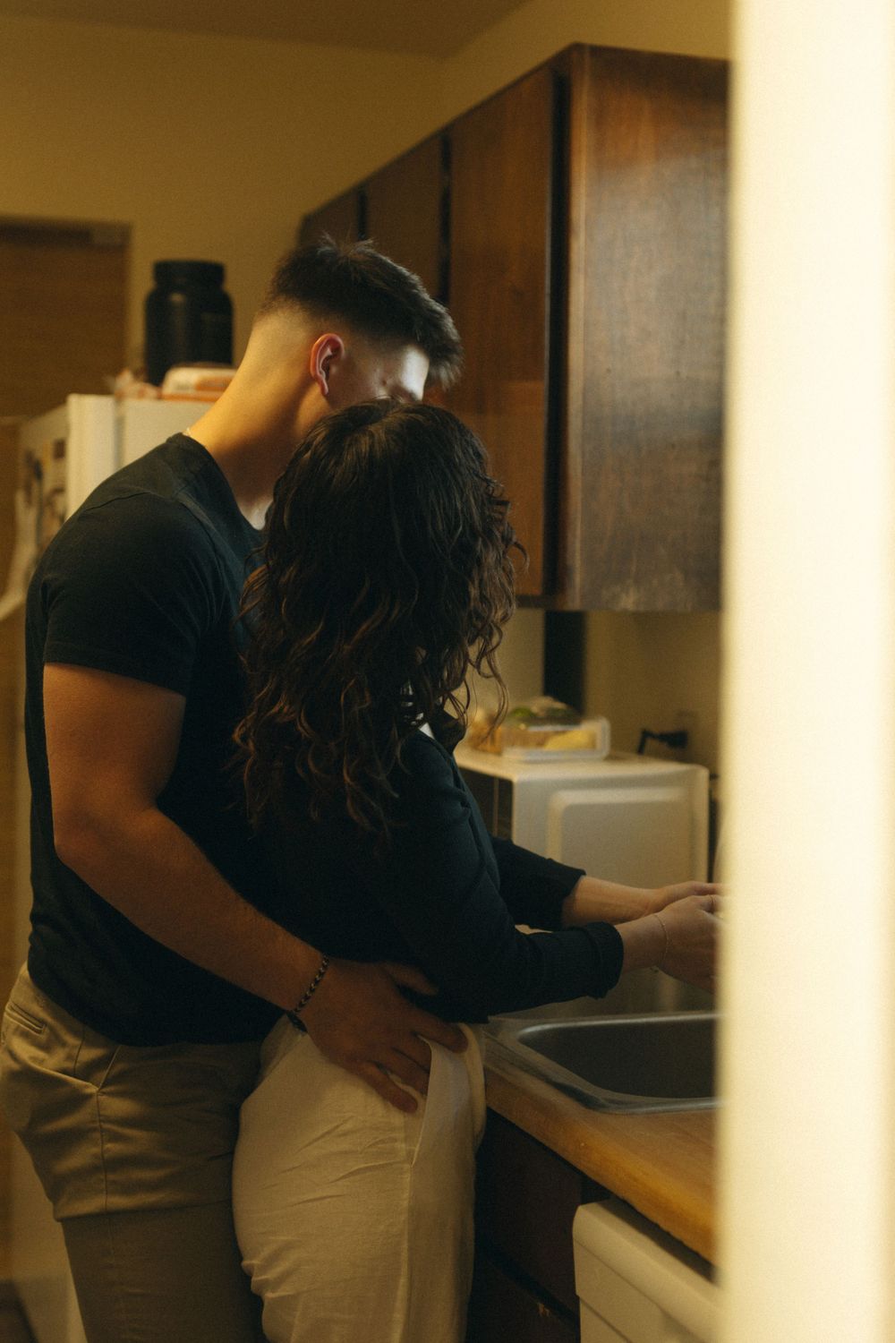 Intimate moment captured in a warm-lit kitchen with natural documentary style photography. In home couple session