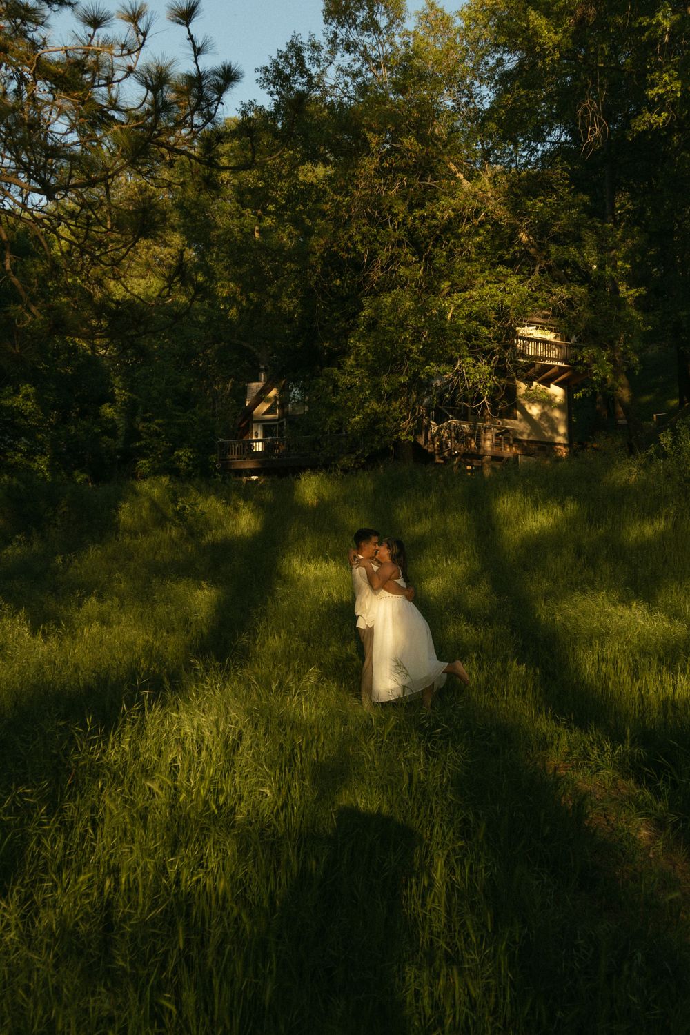 A person in a white dress sits in a sunlit meadow surrounded by trees at golden hour. Documentary photographer