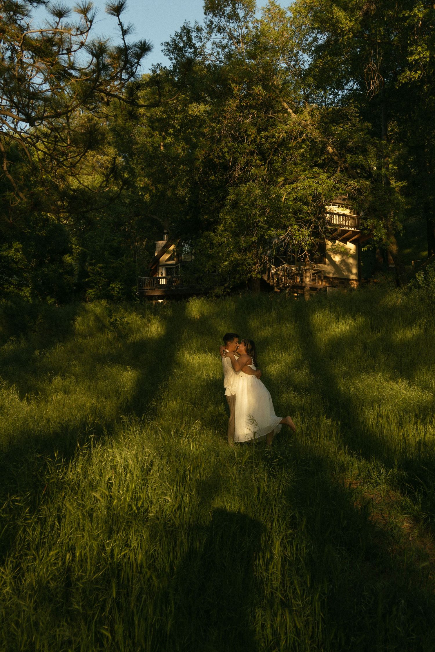 A person in a white dress sits in a sunlit meadow surrounded by trees at golden hour. Documentary photographer