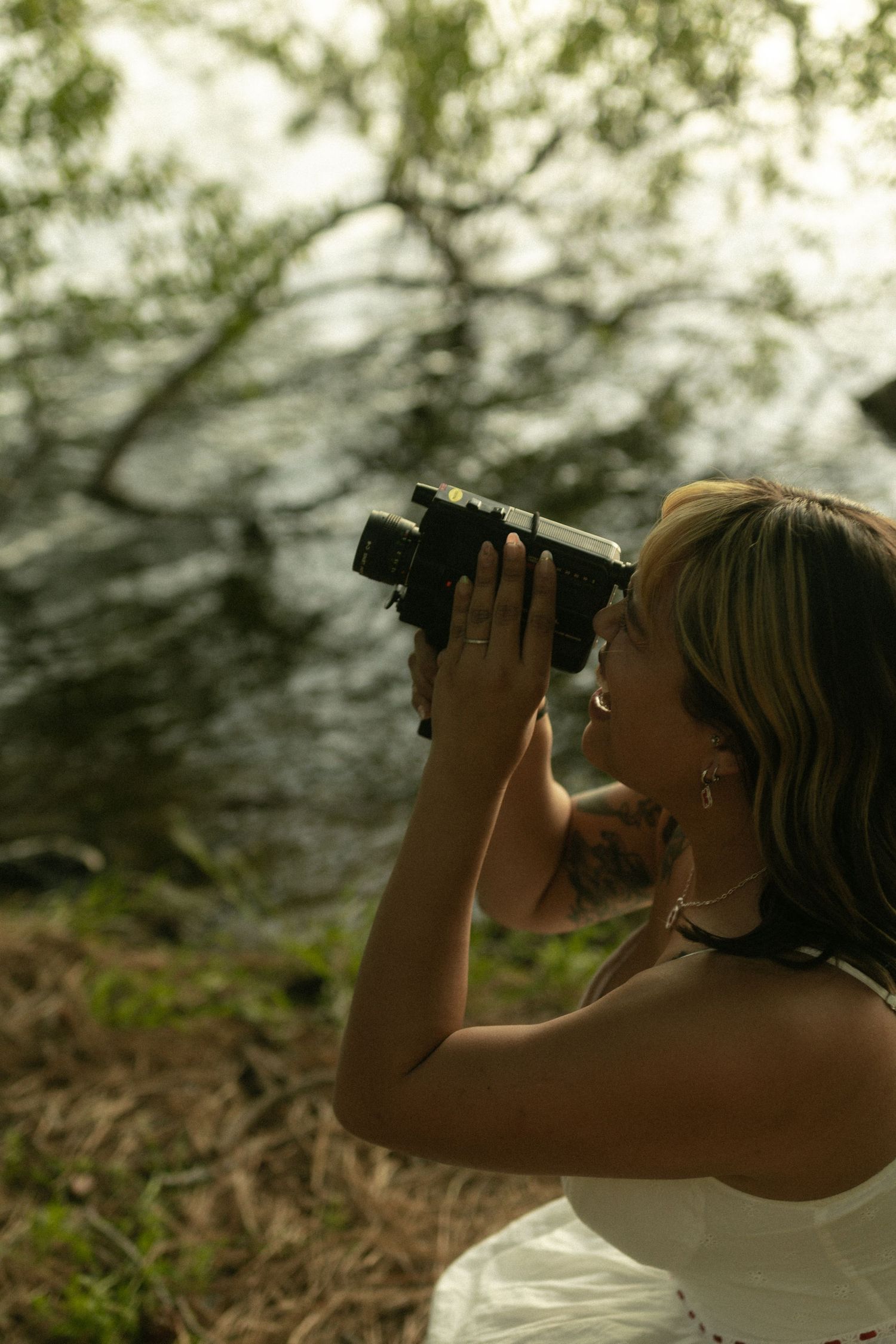 A person in a white dress takes photographs in a natural outdoor setting with super8 camera. Documentary photographer