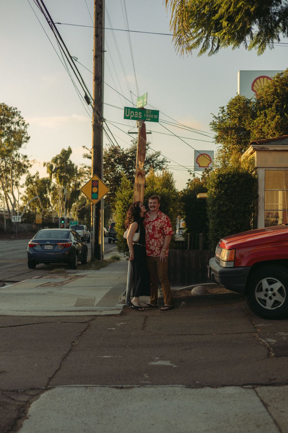 Street corner scene at dusk with parked cars and utility poles. Documentary photographer