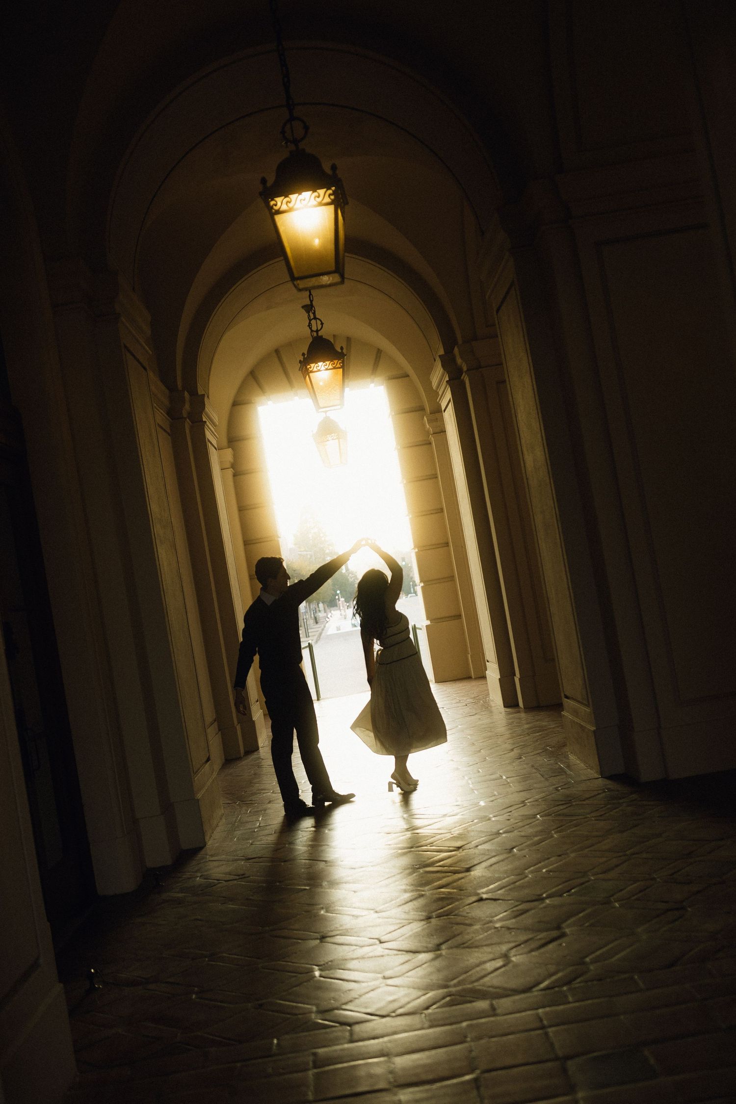 Silhouettes dance in an illuminated arched hallway with vintage hanging lanterns casting warm glows. Documentary photographer