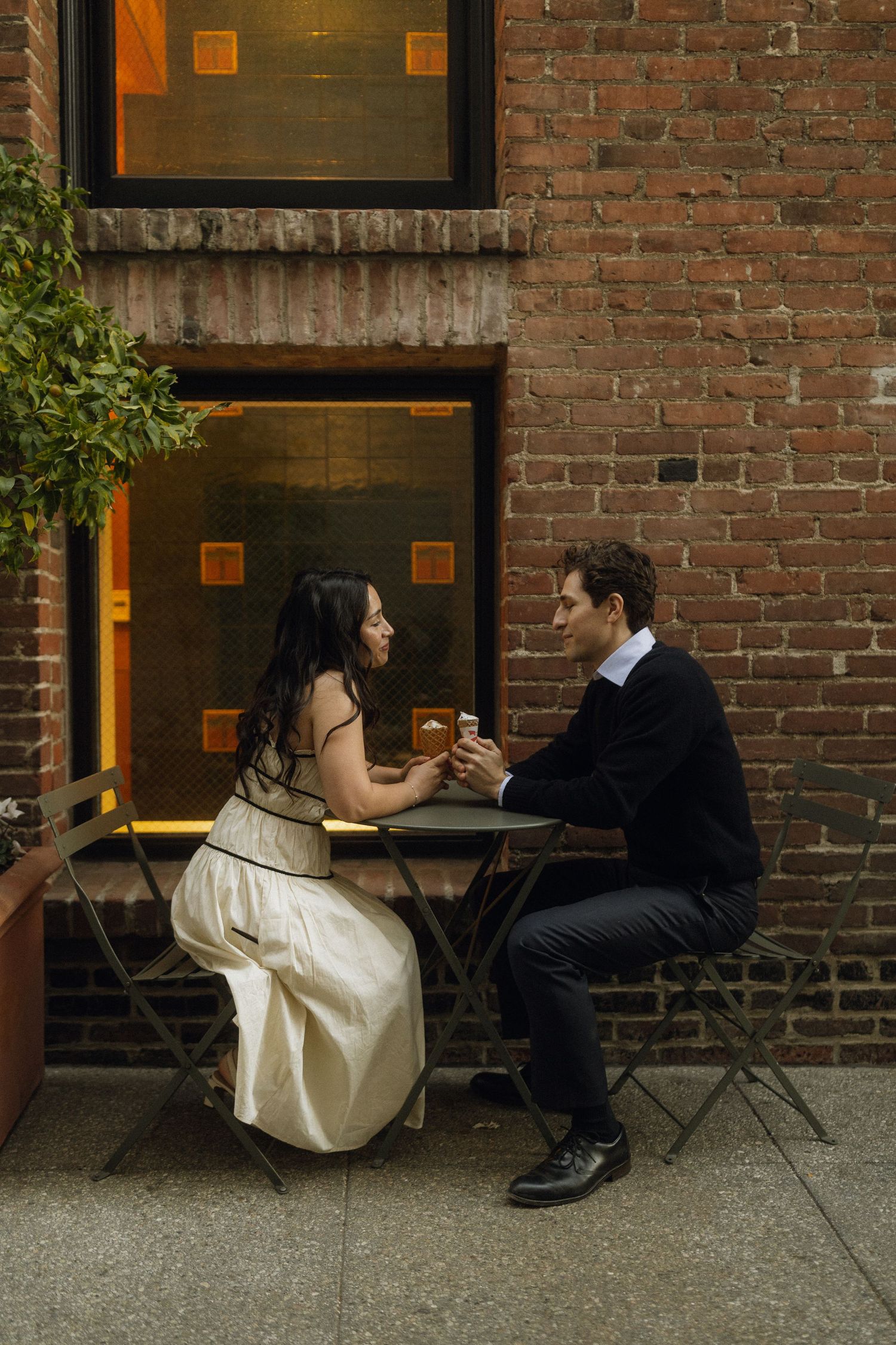A couple shares an ice cream during an  intimate moment at a rustic table against a brick wall backdrop. Documentary photographer