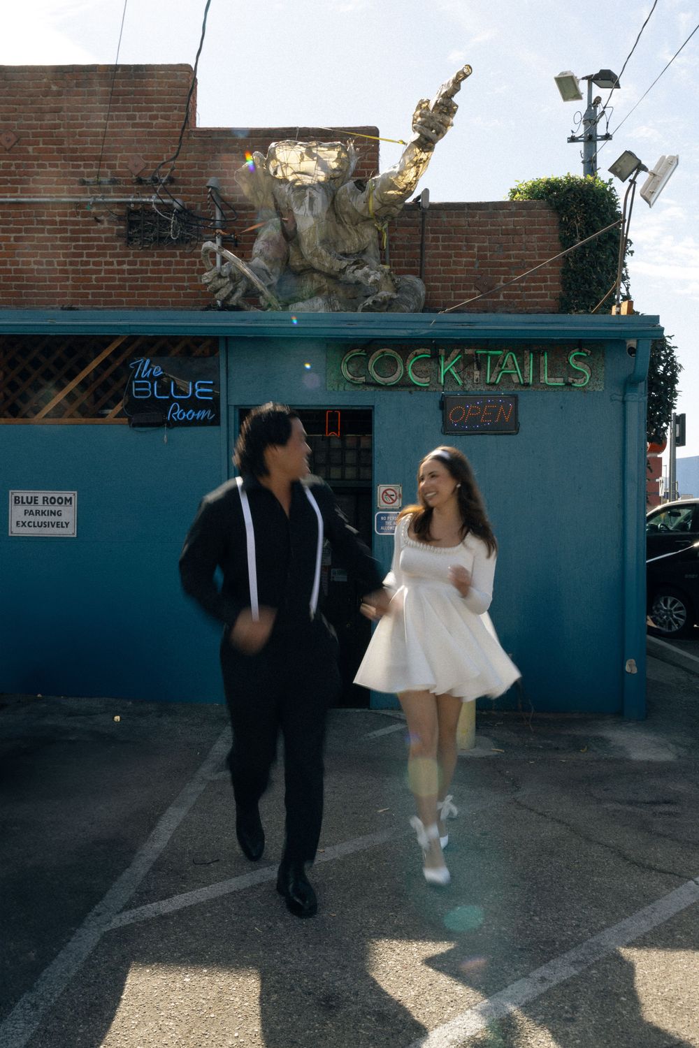 A couple walking outside a blue cocktail bar with decorative sculpture on the roof. Documentary photographer
