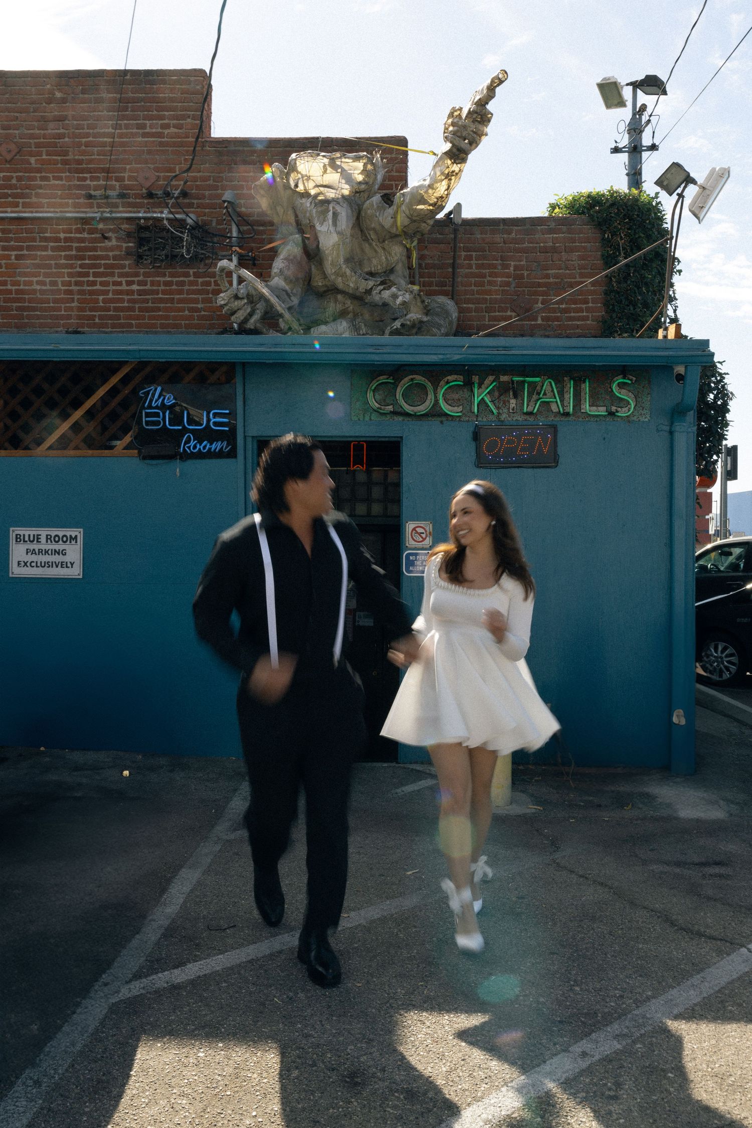 A couple walking outside a blue cocktail bar with decorative sculpture on the roof. Documentary photographer