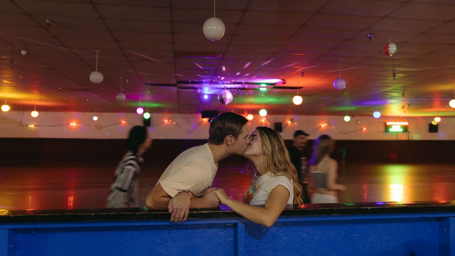 Playful couple leaning over pool table under colorful party lights in a bar setting. Roller skating Documentary photographer