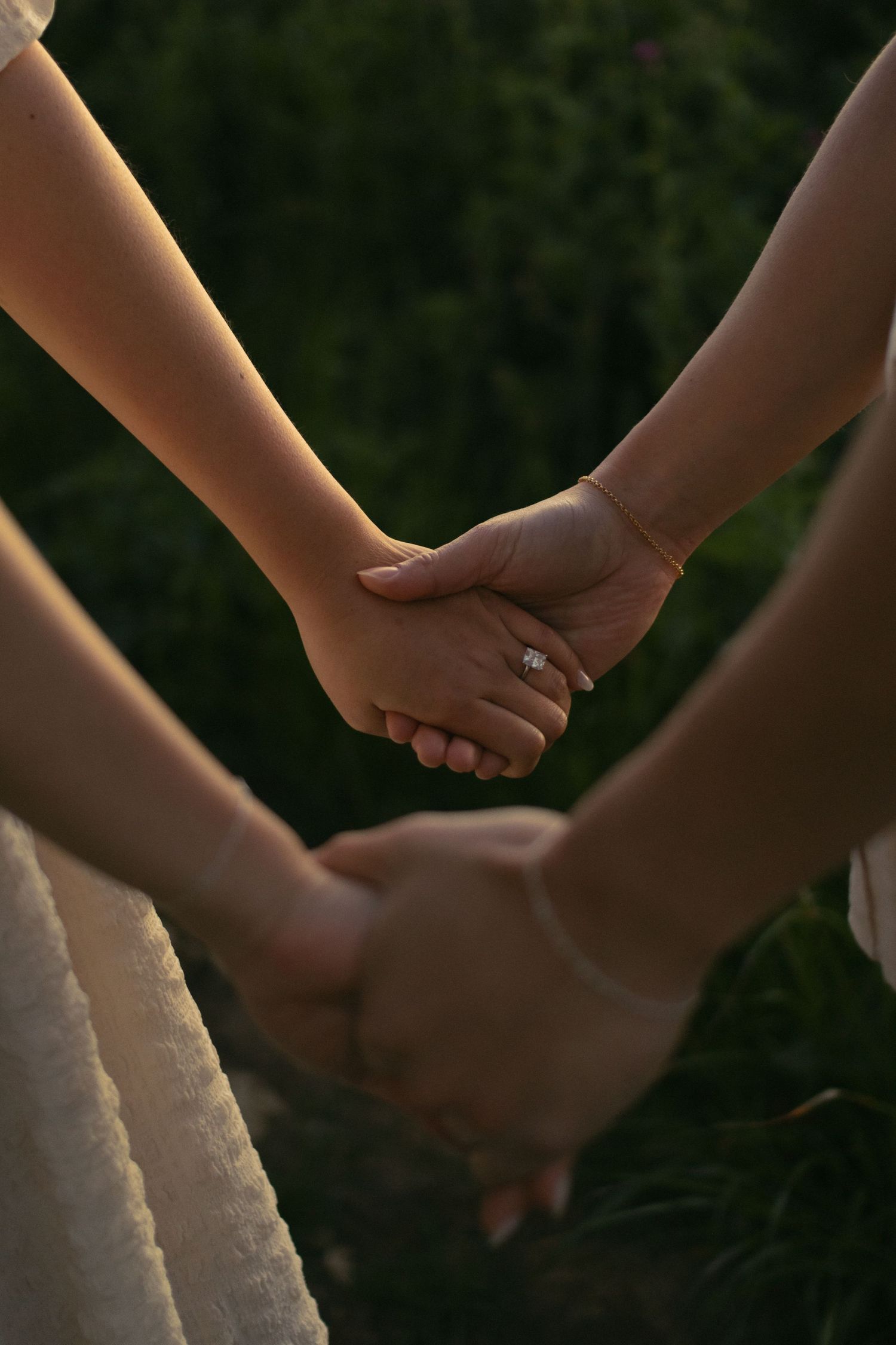 Close-up of hands joined together against a natural green background in evening light. Documentary photographer