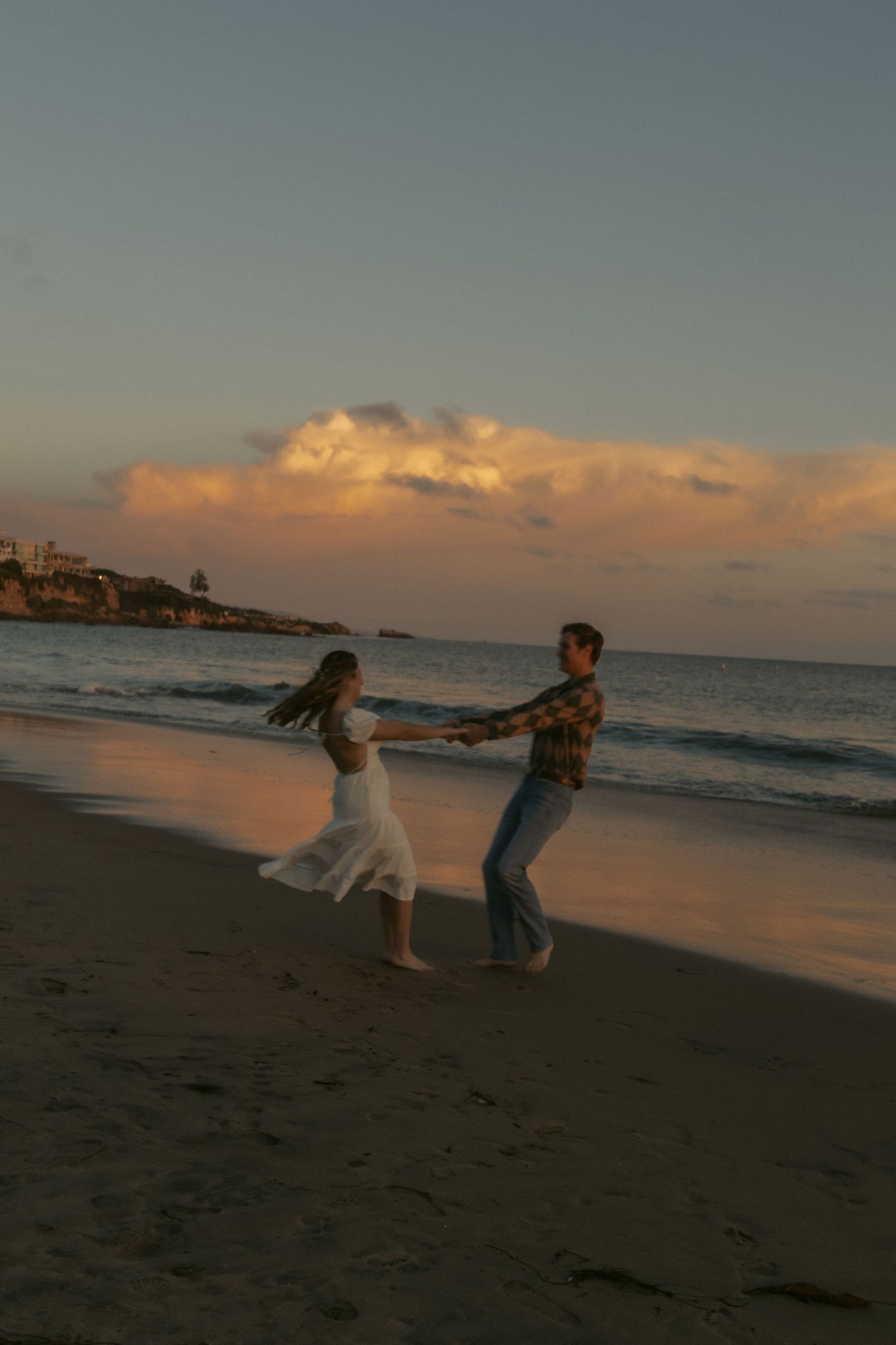 Couple dancing on beach at sunset with golden clouds and waves in background. Beautiful sunset. with natural documentary style photography.