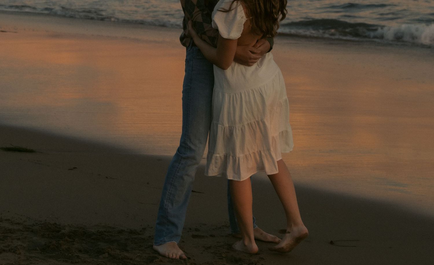 A couple's feet walking together on a beach at sunset with warm orange tones reflecting on the sand. with natural documentary style photogra