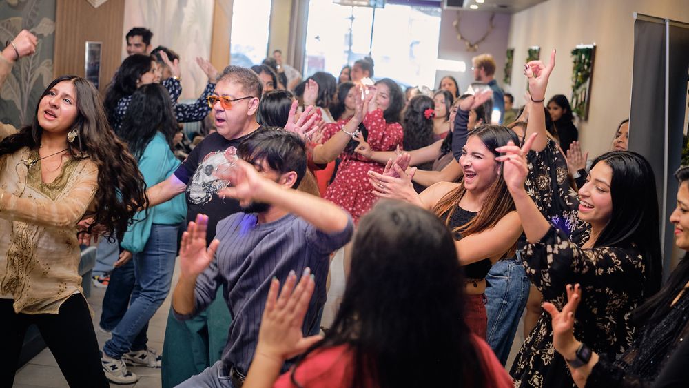 Crowd of people dancing and singing enthusiastically at an indoor event with their arms raised in celebration.