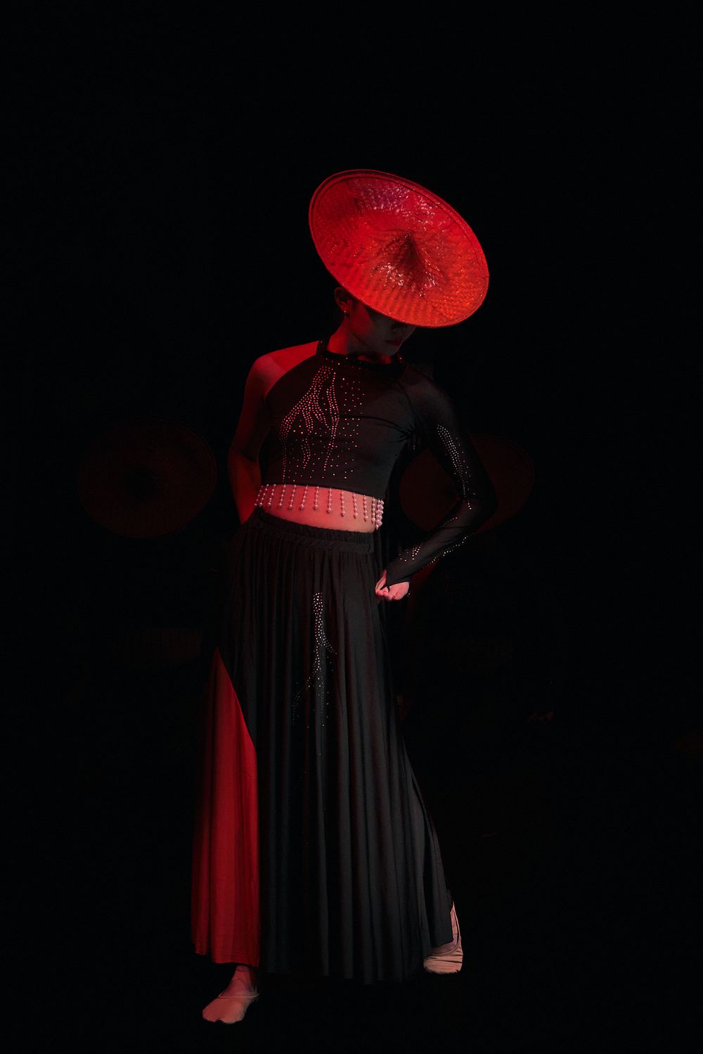 Dramatic silhouette of a figure in black clothing with a red parasol against dark background.