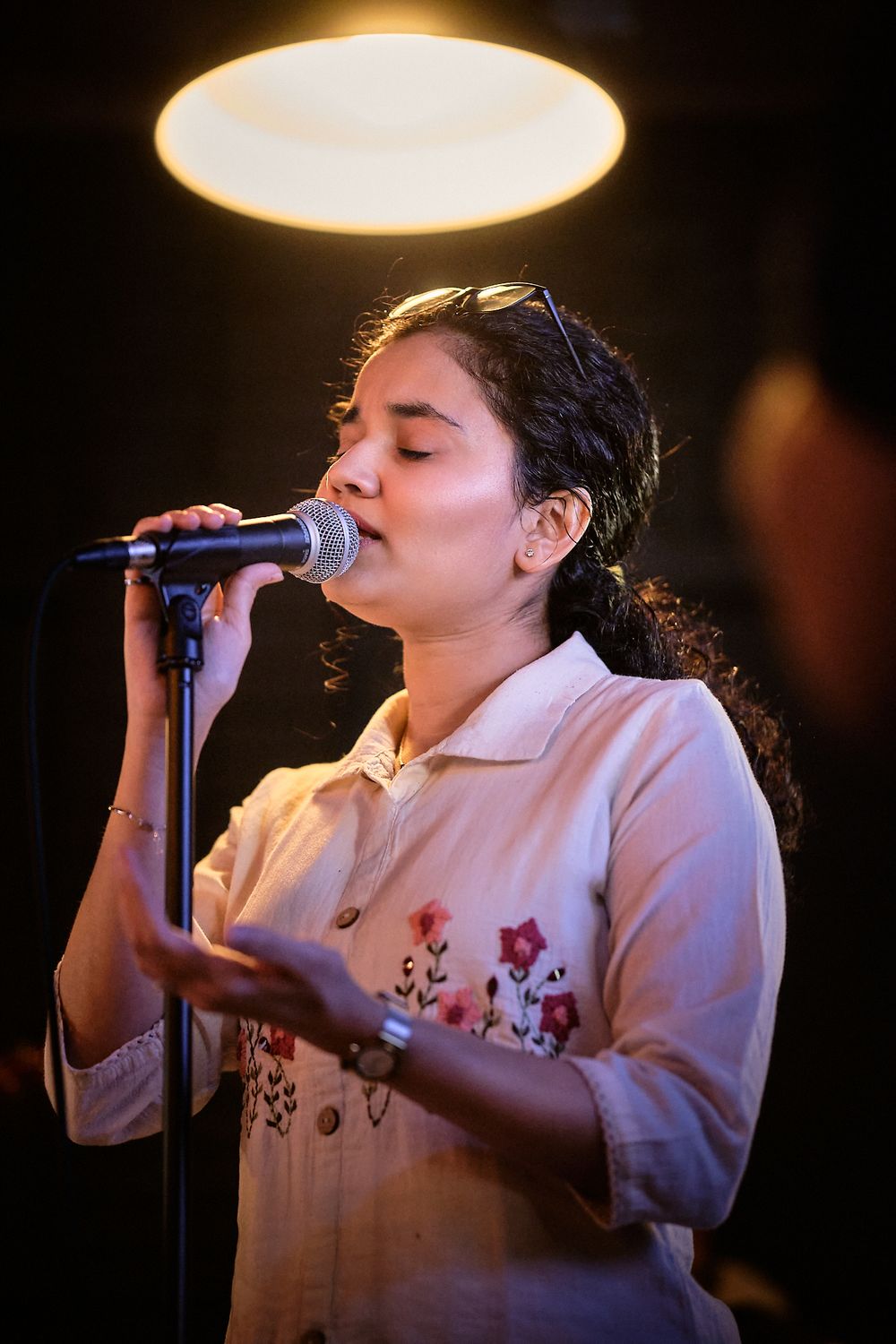 Singer performs passionately on stage wearing a white embroidered top against dark background in sequence of dynamic poses.